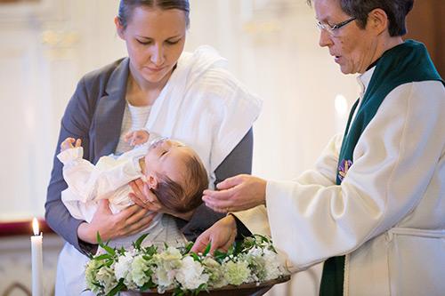 Pappi kastaa pienen lapsen, joka on kummin sylissä.